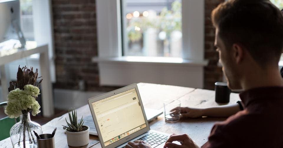 Man writing an email on a laptop at a sunlit desk