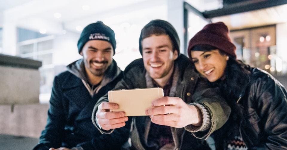 Three friends smiling while filming themselves on a phone