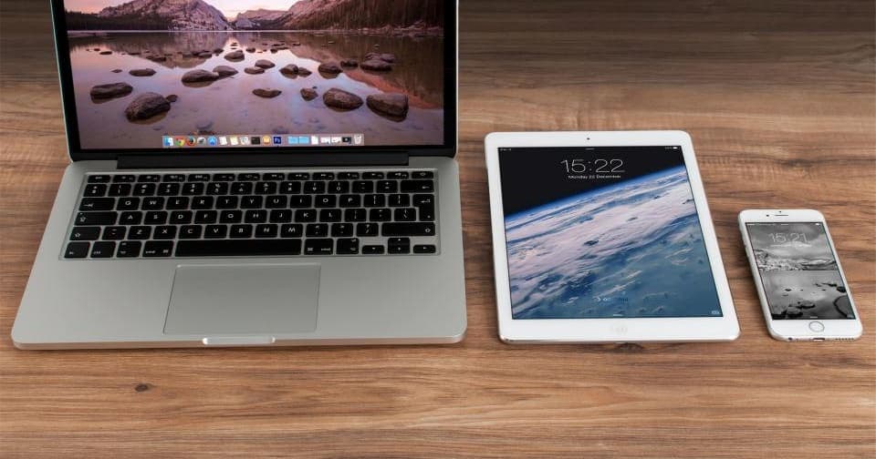 Laptop, tablet, and phone side by side on a wooden desk
