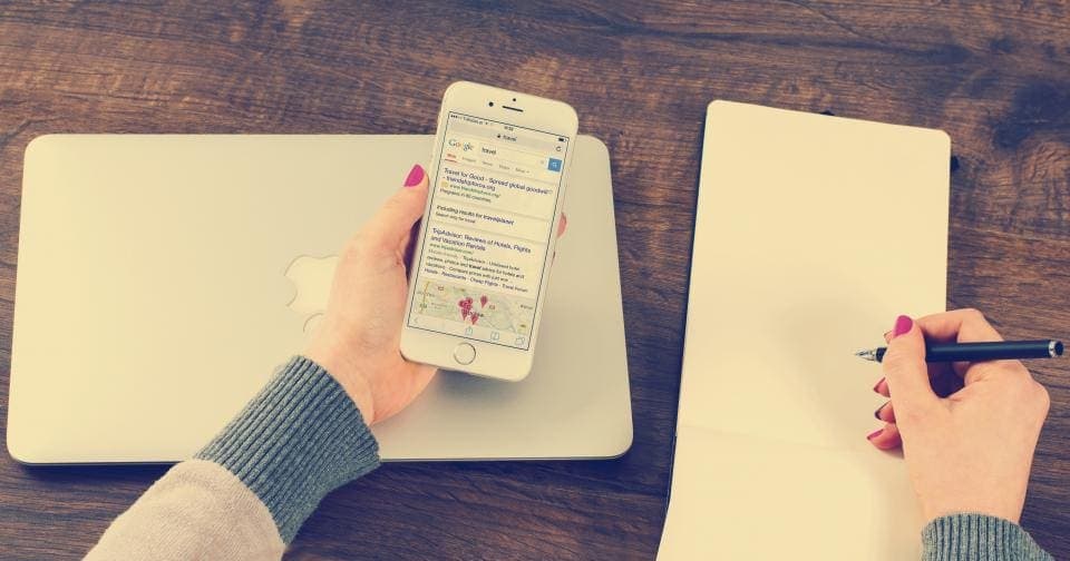 Hand holding a phone showing search results next to a laptop
