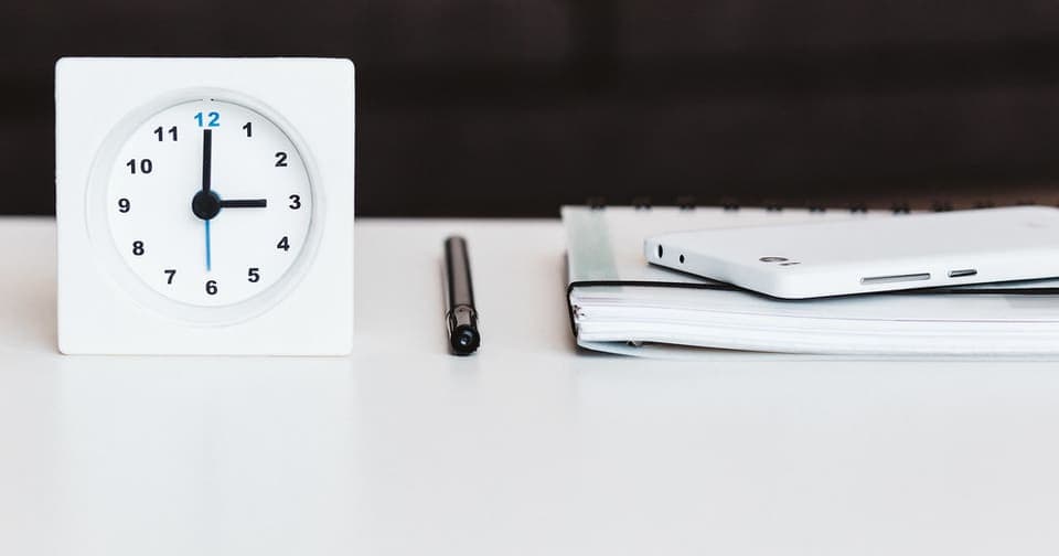 Desk clock next to a pen, notebook, and phone on a white desk