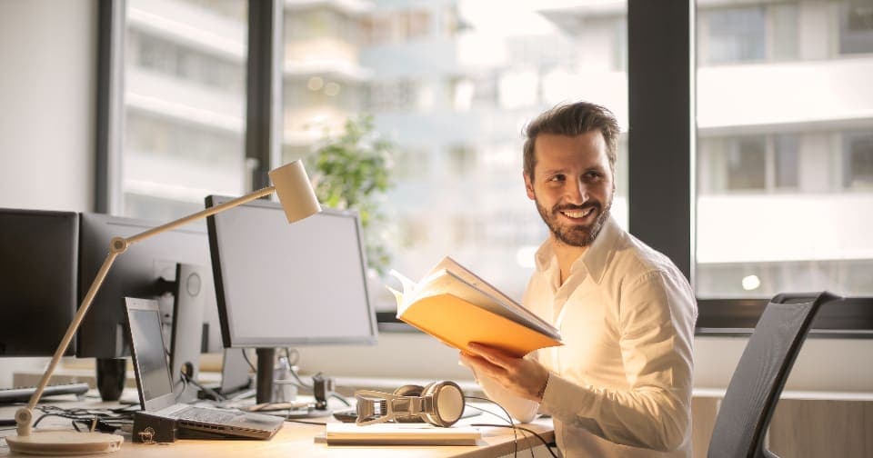 Smiling man holding a notebook at his office desk